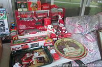 Photo showing a large collection of Coca Cola memorabilia including trays, polar bear figurine, Santa Claus figurines, and boxed collectible train sets.