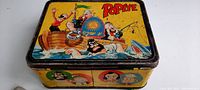 Photo of top and side of metal Popeye lunch box with cartoon characters, showing color and wear