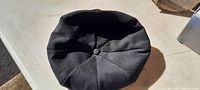 Top view of the black cloth cap showing six-panel construction and central button detail.