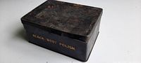 Closed black metal tin container with label 'BLACK BOOT POLISH', showing surface wear and age marks.
