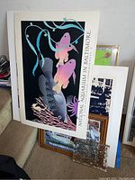 Stack of framed boards and artworks including a large National Aquarium in Baltimore board with colorful fish art on black background and white border