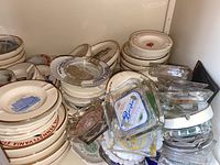 Photo showing stacked ceramic ashtrays with travel and restaurant logos along with clear glass ashtrays with printed ads on top