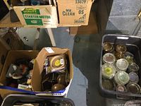 Cardboard boxes and plastic bins holding ashtrays, wood feet, pans, and other items.