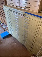 Full frontal view of beige metal blueprint storage cabinet with fifteen drawers, showing physical environment and floor area.