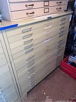 Front angled view of the large metal fifteen-drawer blueprint storage cabinet showing drawer handles, label holders, and surface wear.