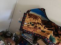 View of painted wall hanging featuring buffalo figures in desert landscape with blue sky and stylized border.
