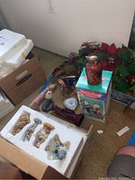 Photo of boxed Christmas figurines including scarecrow and animal figures inside styrofoam package with additional items in background.
