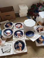 Collection of decorative collectible plates with Marilyn Monroe portraits and other artistic renditions in white protective packaging.