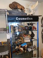 Full view of glass display case with assorted figurines including buffalo, giraffes, cranes, and more, plus decorative lighters and paperweights.