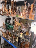 Shelves filled with various giraffe figurines made of wood, brass, glass, and ceramic along with a green glass elephant figurine with chipped tusk