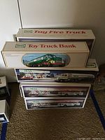 Stack of eight Hess toy truck and bank boxes, front showing and stacked on carpet.