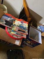 Close-up photo showing three Lionel Classic Series toy trains packaged, placed on a box with a Mickey Mouse trash bin and other collectibles in the background.