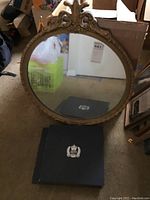 Full view of antique round mirror with carved frame and black presentation box with crown emblem.