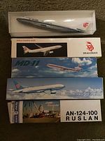 Photo showing Airbus A330 model airplane by Dragonair with MD-11, AN-124-100 Ruslan and Royal Air Force boxed models stacked below, and a plastic model airplane on top