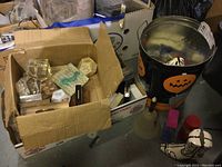 Box filled with various plastic and glass paperweights shown with Halloween tin and snow gloves nearby.