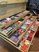 Three drawers full of assorted playing card decks, each with various themes and box designs.