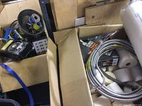 Photo showing open cardboard boxes containing rolls of tape, receipt tape, flexible metal wiring coils, a black rotary vintage phone, and some electrical hardware scattered inside the boxes.