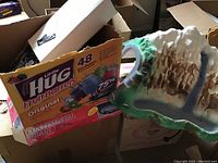 Styrofoam mountain tunnel with painted landscape details alongside boxed items and track pieces visible in an open cardboard box, showing lot contents and condition.