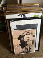 Stack of framed wall art pieces including a black frame with a signed photo of Babe Ruth and Lou Gehrig visible at the front.