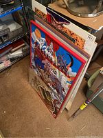 Stack of posters leaning against a wall, showing size range and edges of several artworks including an anime themed poster.