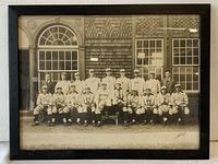 Full framed team photo showing entire baseball team and coach posed outside a building with large windows and shingled siding.