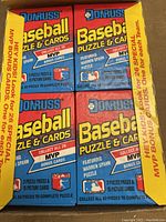 Box filled with multiple sealed wax packs of Donruss 1989 baseball cards and puzzle pieces with MVP bonus cards text on yellow strip.