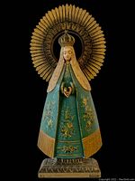 Front view of the full statue showing green painted wooden Madonna with floral details and large halo on black background