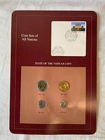 Front view of the Franklin Mint Coin Set of Vatican City coins displayed on burgundy background with four coins and a postally-cancelled Vatican City stamp