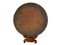 Full front view of round handmade copper dish with three moth motifs and hammered border.
