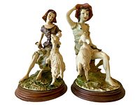 Pair of Capodimonte Salci figurines showing both the female and male figures seated with goats mounted on round wooden bases.