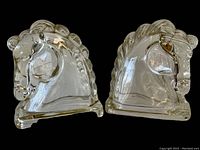 Pair of transparent glass horse-head bookends side by side on a black background showing front detail and reflective surfaces.