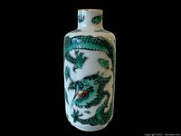 Front view of small white cylindrical ceramic vase featuring a green dragon painted design with red accents around mouth, and cloud motifs.
