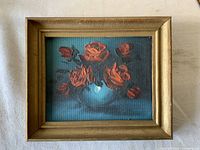 Front view of small vintage oil painting on board showing floral still life with orange-red roses and teal background in gold-toned frame.