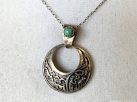 Front view of sterling silver crescent pendant with turquoise stone, showing detailed engraving and chain attachment.