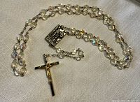 Full length view of the rosary showing faceted iridescent beads, rectangular centerpiece, and crucifix marked Italy.