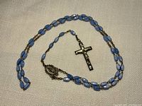 Full view of the rosary laid flat showing the blue glass beads, metal crucifix, and religious medal.