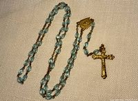 Full view of vintage translucent blue glass bead rosary laid flat showing entire length and details of beads, centerpiece, and gold-tone crucifix.
