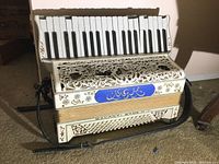 Full front view of the Galanti Bros. vintage accordion showing ivory color, keyboard, bass buttons, and blue MGK panel.