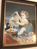 Framed print of child with toy lambs on wheels in natural tone frame.