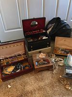 Wide shot of three open jewelry boxes (red, black, wooden) on floor with assorted jewelry pieces
