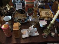 Photo shows overall table display with all items present including glass decanter, tiger tin, cat plate, brass candle holders, decorative bowl, framed art.