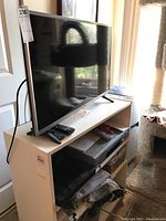 Wide view showing LG TV on stand with remotes and shelf with other electronics