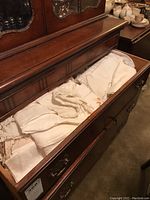 Drawer of dresser containing folded white and cream-colored linens including embroidered tablecloths and napkins.