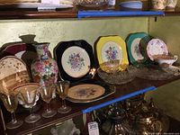 Multiple decorative plates, cordial glasses, vase, and serving dish arranged on wooden shelves