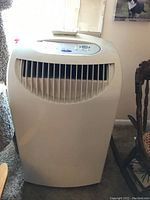 Front view showing the white plastic portable air conditioner with air vent grill and top controls.