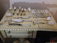 Assorted flatware laid out on table showing knives, forks, spoons, cocktail forks and serving utensils