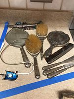 Overview of lot including silver-plated mirror, two brushes, comb, magnifier loupe, snake-chain necklace and red stone clips