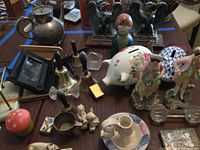 Overall view of the lot showing metal teapot, eagle bookends, piggy banks, figurines, bells, and smaller items.