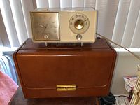 Zenith Trans Oceanic radio in brown leather carrying case with gold-tone clasp and GE plastic clock radio on top.