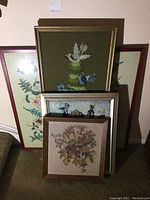 Five framed wall art pieces stacked showing different needlepoint designs including floral and bird motif